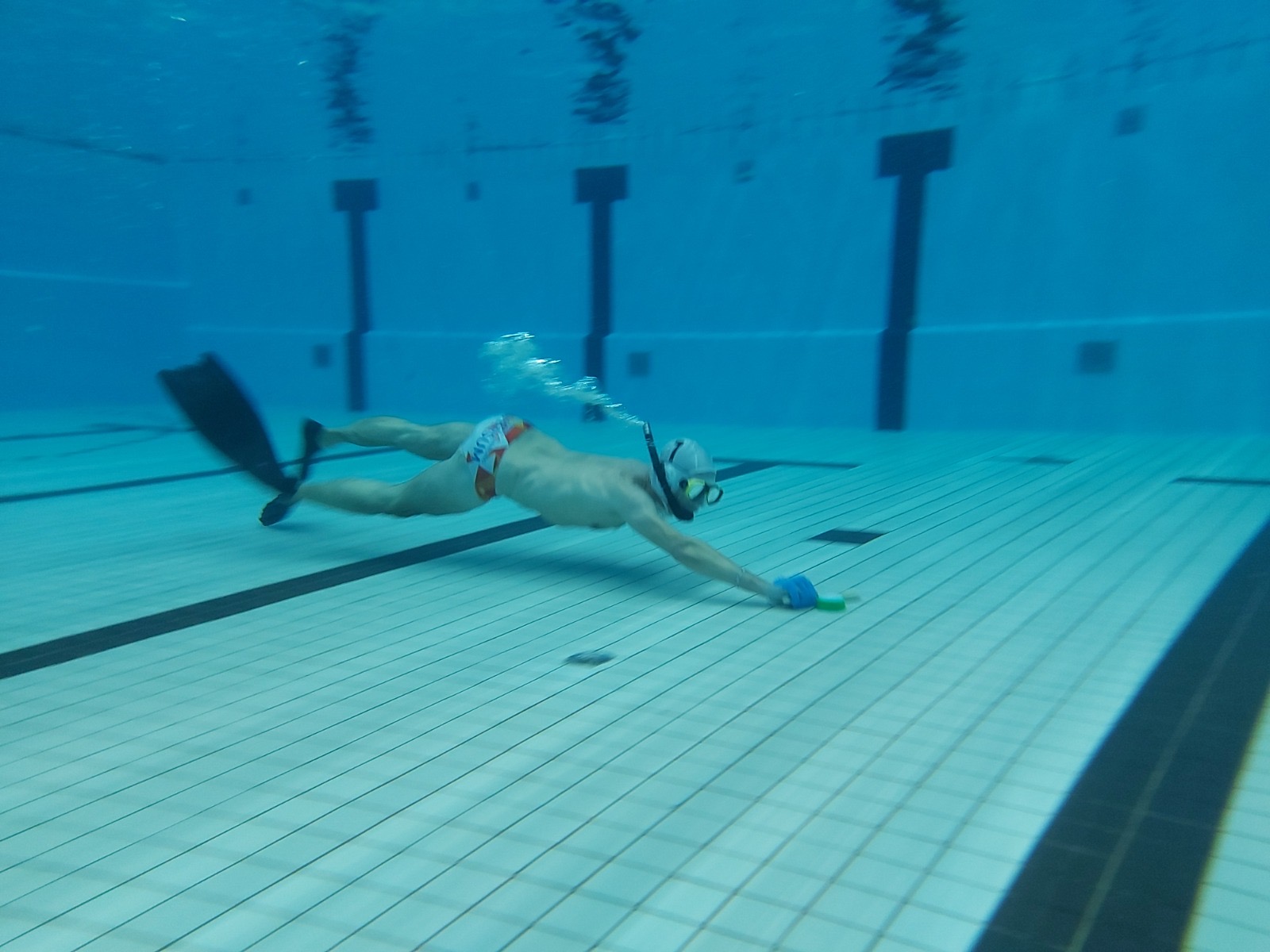 Onderwaterhockeyspeler duikt met stick naar de puck op de bodem van het zwembad